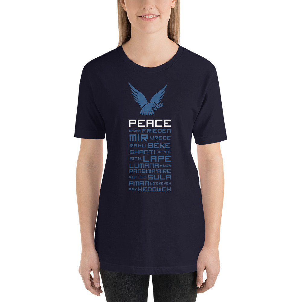 Female model wearing a fashionable graphic t-shirt featuring a dove, the symbol of peace, then the word "Peace," and then the word Peace in various languages from around the world, all in a stacked, jenga arrangement.