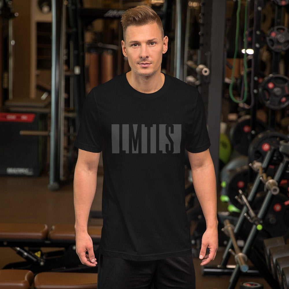 Man in a gym wearing a stylish graphic t-shirt featuring the word "Limitless" dropped out of a solid gray block and stylistically spelled "LMTLS."