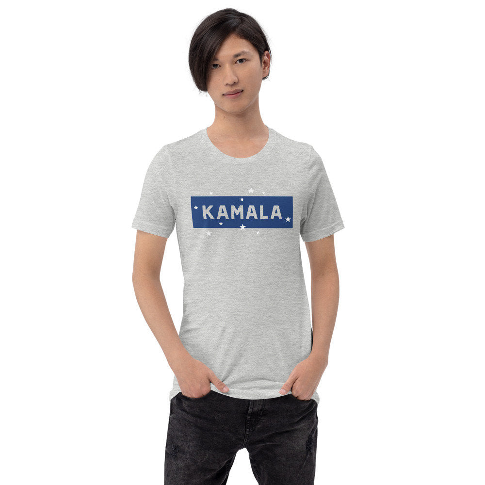 Model wearing a graphic t-shirt reading "KAMALA" within a blue block, peppered with white stars, marking her nomination for Vice President of the United States, and now celebrating her win with Joe Biden as President.